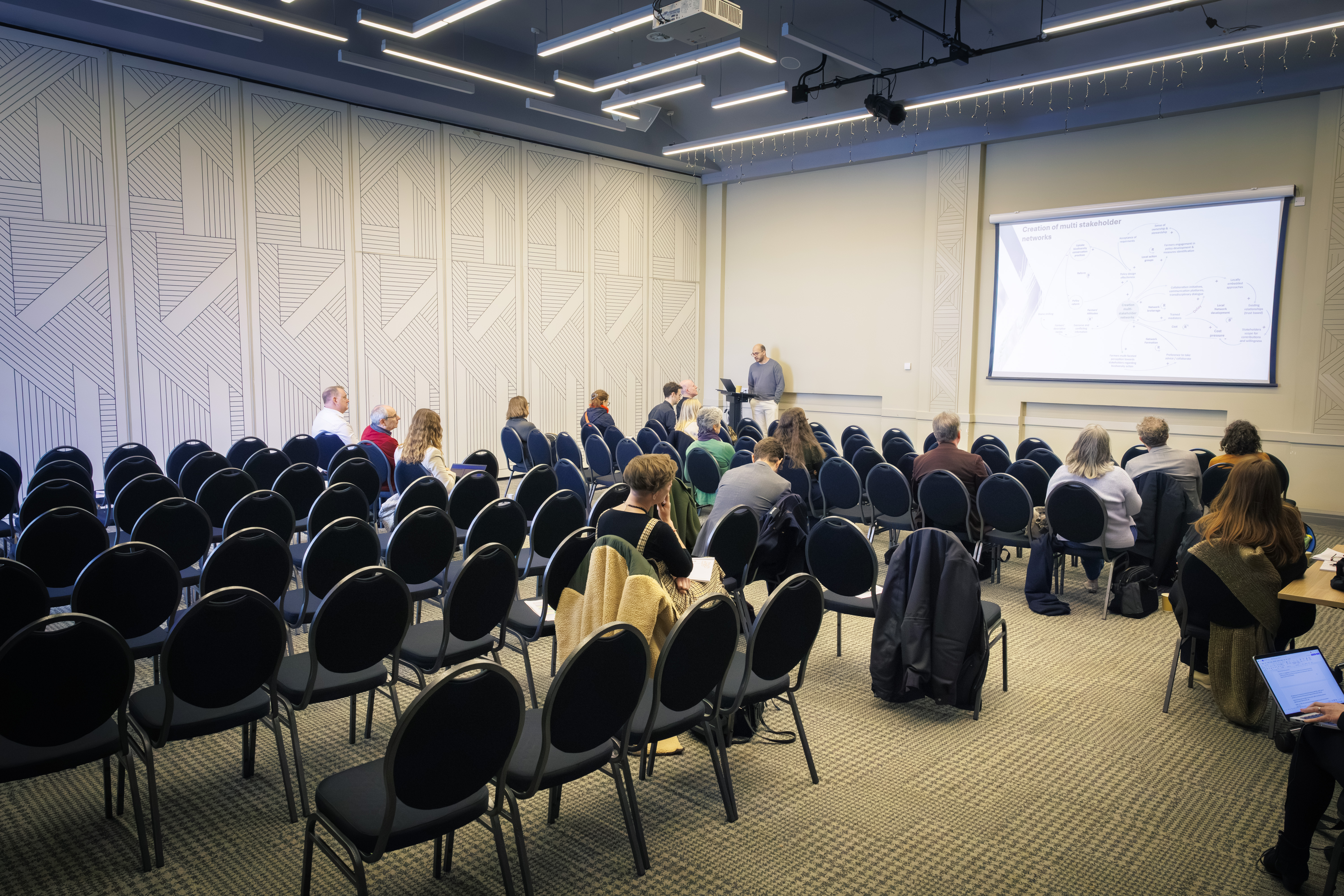 A handful of people watch a session in a large conference room that's been partitioned in half