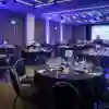 A large room with mood lighting, with circular tables set up with formal dinnerware