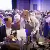 A smiling waitress carefully places a plate of food in front of a laughing man at a conference meal