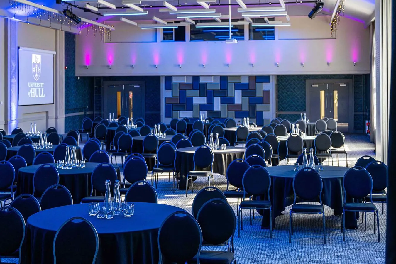 A large room with multiple sets of tables and chairs set up for a formal event
