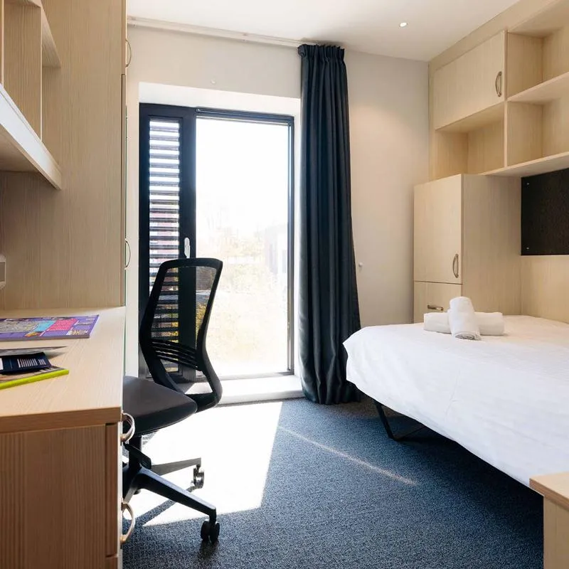 A standard guest room in The Courtyard, with a desk, a double bed and wardrobe.