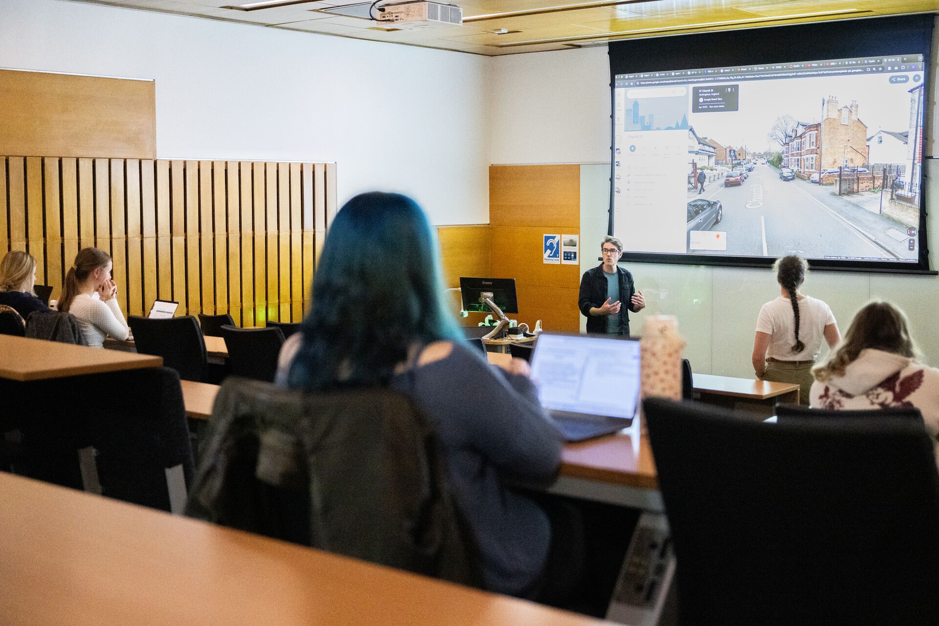 A man gives a presentation in a small wood panelled lecture room