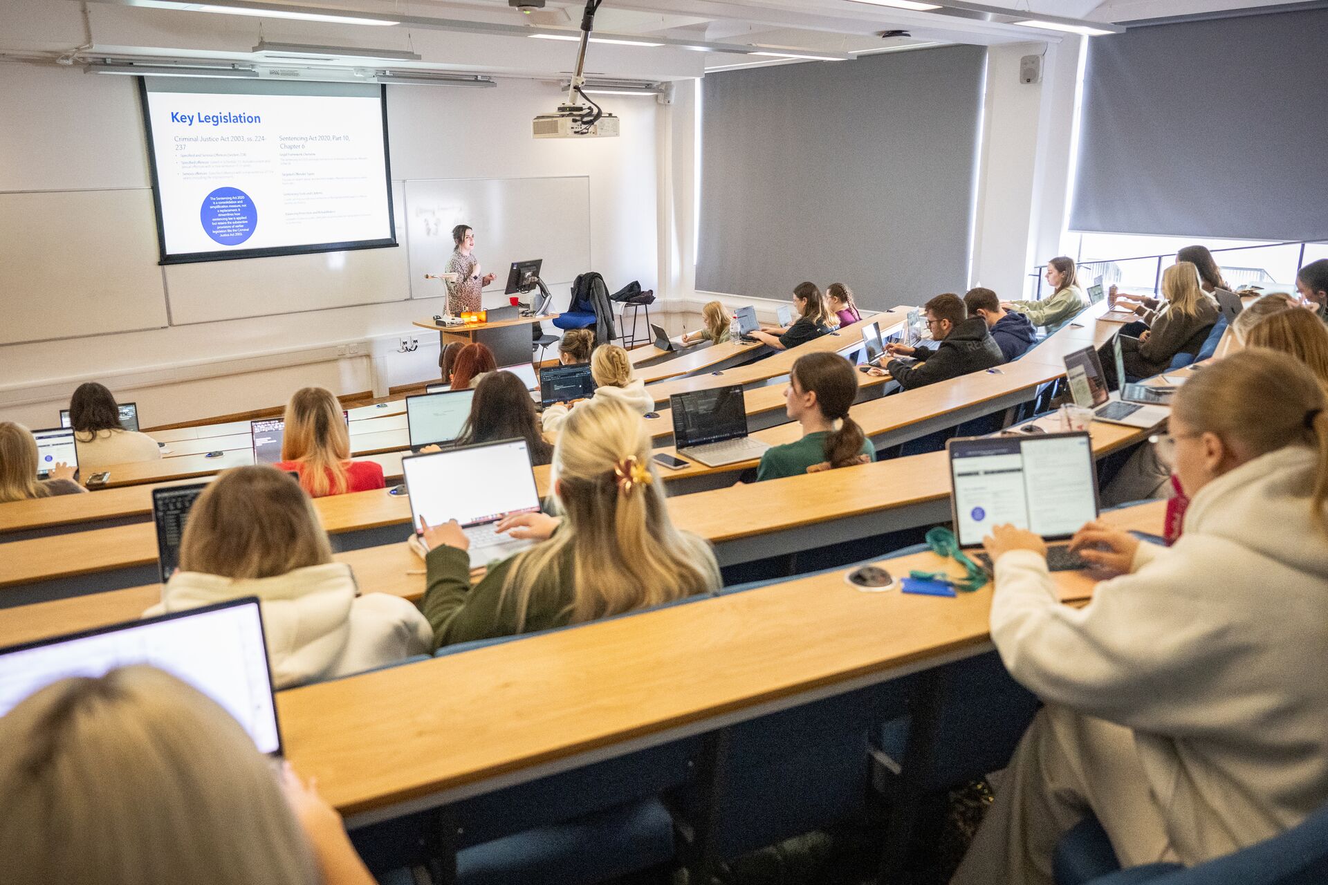 Students sit in rows in a banked lecture theatre