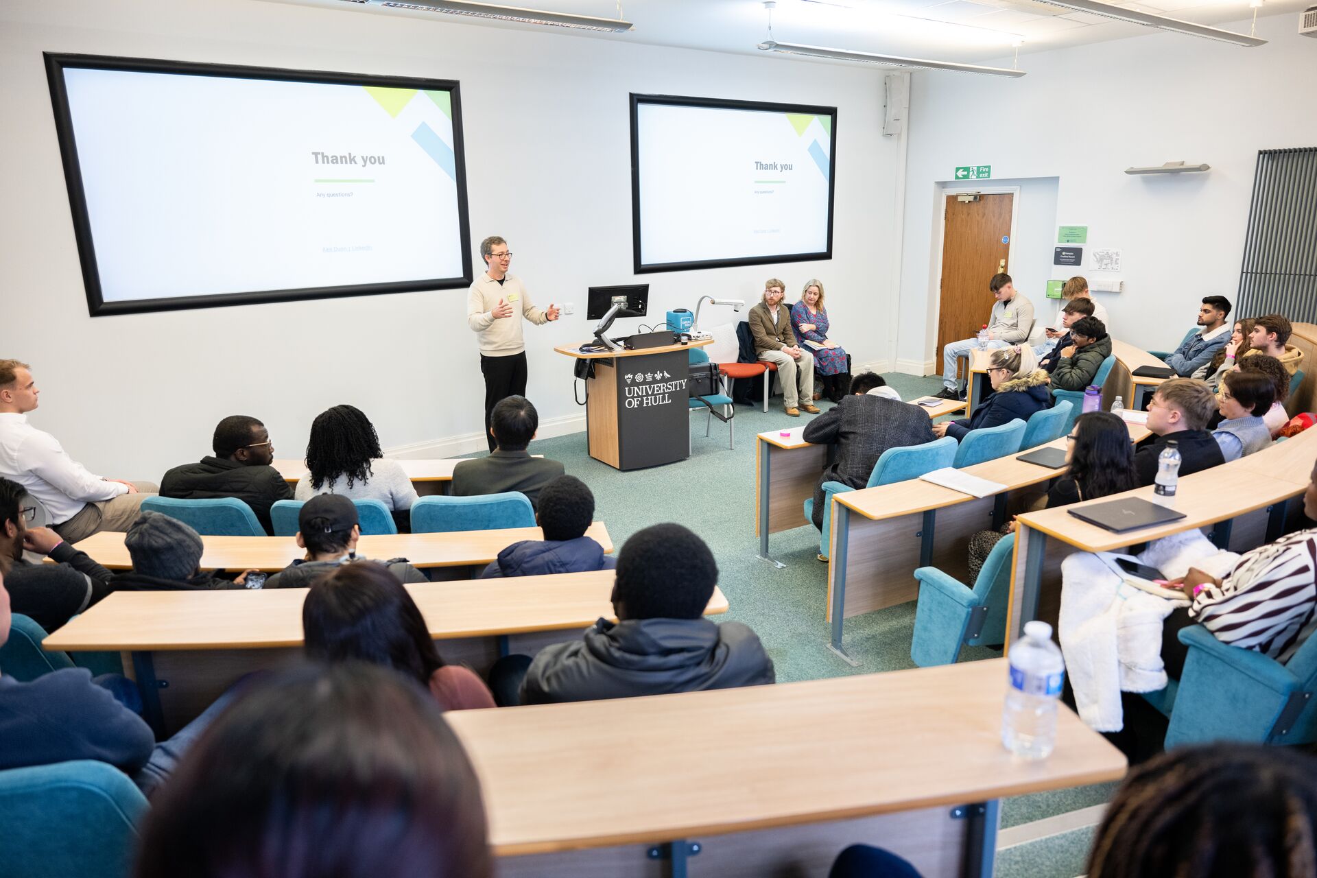 A man gives a talk in a small lecture theatre to a group of students