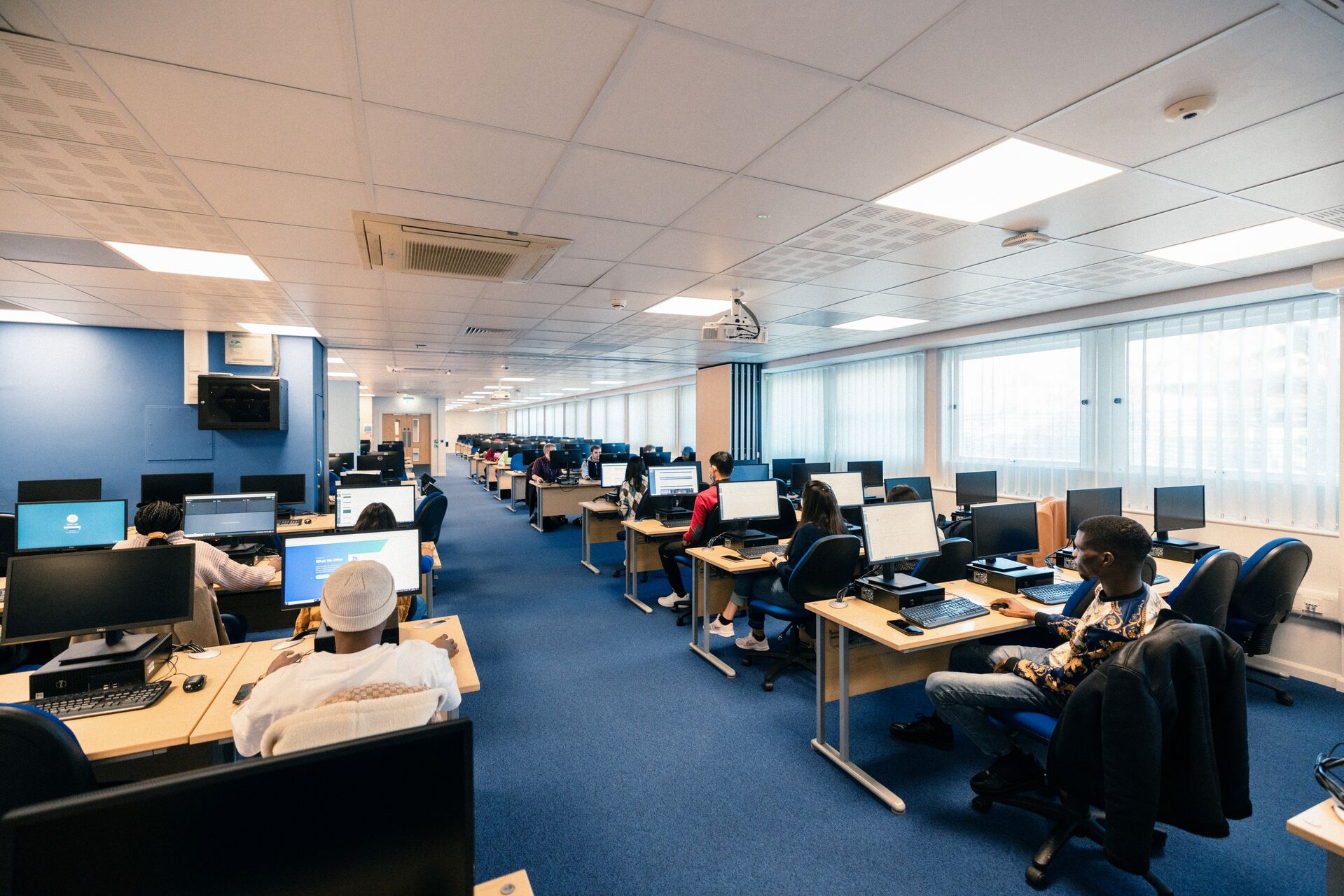 A large, modern computer suite with students sitting at banks of PCs